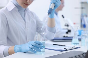 Fototapeta premium Scientist dripping sample into beaker in laboratory, closeup