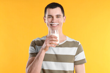 Happy man with milk mustache holding glass of tasty dairy drink on orange background