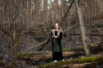 A young woman with a mobile phone stands on a green mossy tree trunk in the forest, early spring