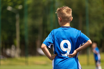 Boy playing soccer with teammates. The soccer boy plays as a forward. Kids soccer team in a soccer league match. A child in a blue football uniform with the number nine on back - obrazy, fototapety, plakaty