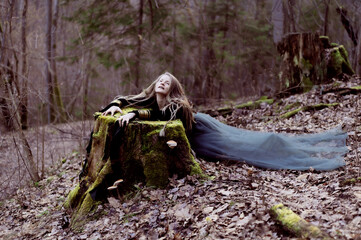 Female shaman in pristine forest nature laying on green tree stump, gold jewelry, shaggy hair