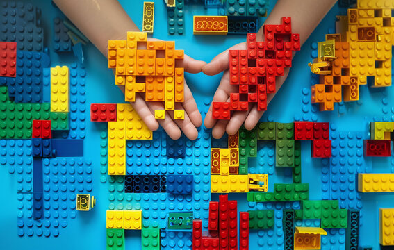 Hands assembling colorful plastic bricks on a blue background, depicting creativity and teamwork in play.