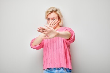 Blonde woman in pink top gesturing stop with her hands against a white background.