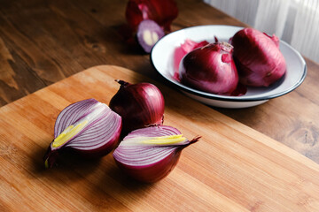 Board and bowl with pieces of fresh red onion on wooden background