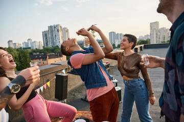 jolly attractive people in stylish outfits pouring tequila in mouth of their african american friend