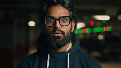 Emotional Indian shocked bearded guy in glasses astonished looking at camera at dark underground...
