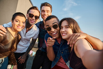 attractive jolly multiracial friends posing together on rooftop and smiling happily at camera