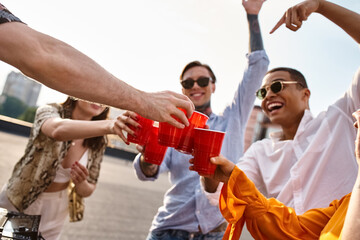 young joyful multiracial friends clinking their red cups next to DJ equipment at rooftop party