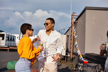 cheerful woman and african american man in urban clothes with sunglasses partying on rooftop