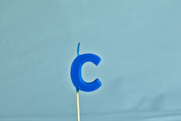 close up on a blue letter C birthday candle on a white background.
