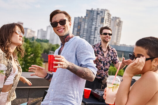 joyful friends in casual attires with sunglasses drinking at rooftop party and dancing to DJ set