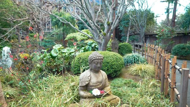 A 4k slow-motion, stabilized video depicting a beautiful buddha statue surrounded by flowers, lush plants and trees in a Japanese Tea Garden in san mateo, california.