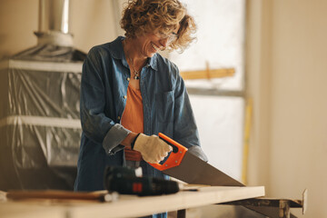 Happy mature woman using crosscut saw for DIY home improvement renovation project