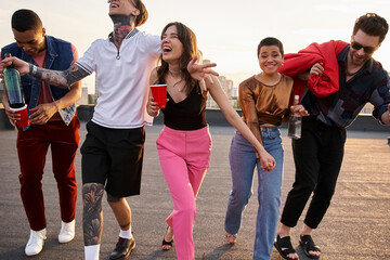 cheerful appealing diverse friends in vibrant outfits holding alcohol drinks and having fun at party