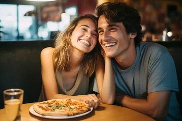 Schilderijen op glas Happy young adult couple have fun eating a pizza together by night in traditional italian pizzeria restaurant sitting and touching romantic. People enjoying food and dating relationship. Tourists © simona