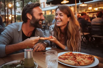 Poster Happy young adult couple have fun eating a pizza together outdoor in traditional italian pizzeria restaurant sitting and talking and laughing. People enjoying food and dating relationship. Tourists © simona