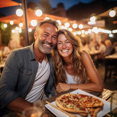 Happy adult cute couple have fun eating a pizza together outdoor in traditional italian pizzeria...