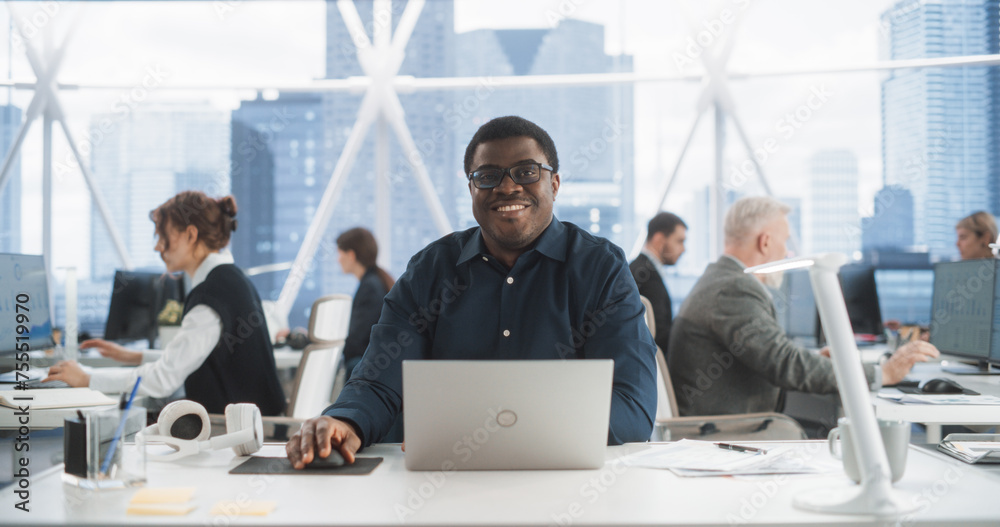Poster Succesful Black Man Typing On Laptop Computer In Bright Scyscraper Office With Diverse Employees In Downtown. Cheerful Male Programmer Looking At Camera And Smiling In Fintech Startup Workspace.