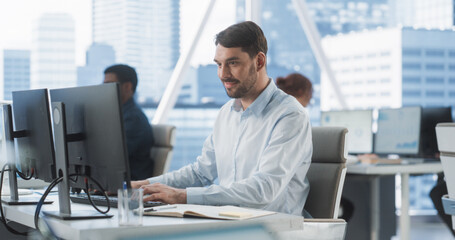 Happy Male Sales Manager Typing On Desktop Computer In Diverse Corporate Office With Megapolis Window View. Proffesional Caucasian Man Smiling After Closing Big Advertising Deal For E-commerce Company
