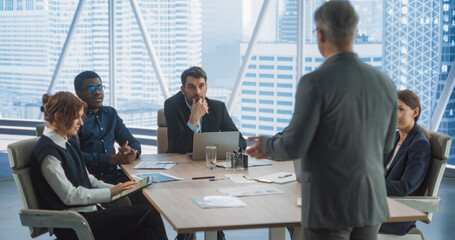 Back View of Caucasian Male Entrepreneur Talking On Board Of Directors Meeting In Corporate Office. Diverse Investors Listening And Discussing With Businessman Growth Strategy For Consulting Company.