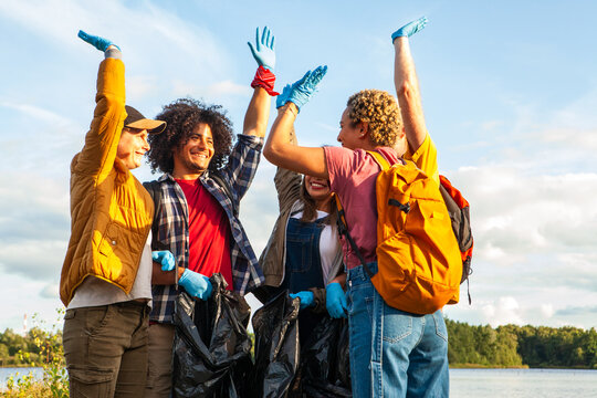 Joyous group of volunteers raising hands in triumph after a lake shore clean-up effort. Ecstatic Volunteers Celebrating a Successful Lake Cleanup. High quality photo - Powered by Adobe