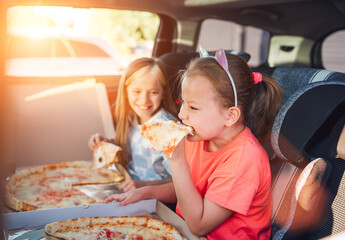 Portrait of two positive smiling sisters eating just cooked italian pizza sitting in child car...