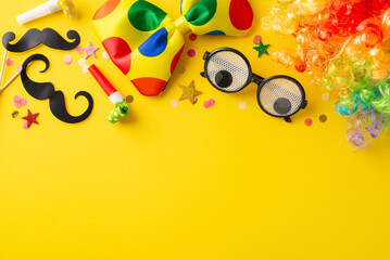 Joyful April 1st top view scene with comic eyewear, a bright clown hairpiece, a quirky bow tie, a stick-on mustaches, party blowers, and confetti on a lemon-hued surface, space for wording
