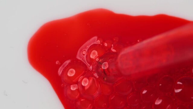 The slow release of a red cosmetic fluid on white, mimicking blood, suggests a laboratory's quest for the elixir of youth.