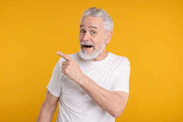 Surprised senior man pointing at something on yellow background