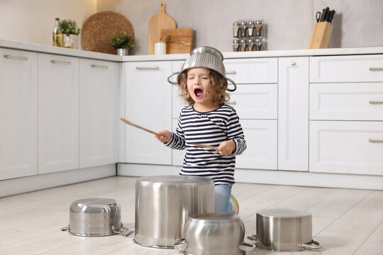 Little girl pretending to play drums on pots in kitchen