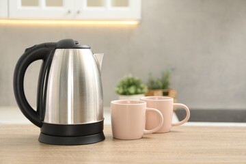 Modern electric kettle and cups on table in kitchen. Space for text