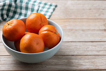 Fresh tangerines in green bowl on wooden table. Copy space