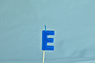 close up on a blue letter E birthday candle on a white background.
