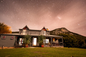 Home with stary skies and mountains behind - obrazy, fototapety, plakaty
