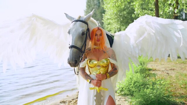 Art video real people woman warrior queen with white horse bird wings pegasus animal. Fairy tale style girl sexy beauty face elf holds sword. Golden armor silk dress. summer nature sun light sky. 4k