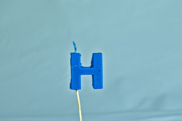 close up on a blue letter H birthday candle on a white background.
