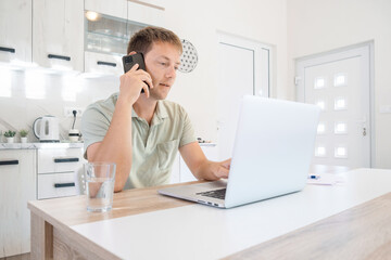 Serious businessman trader talking on phone call while work on laptop at home. Male professional broker investor working online on stock market and crypto currency with smartphone and computer