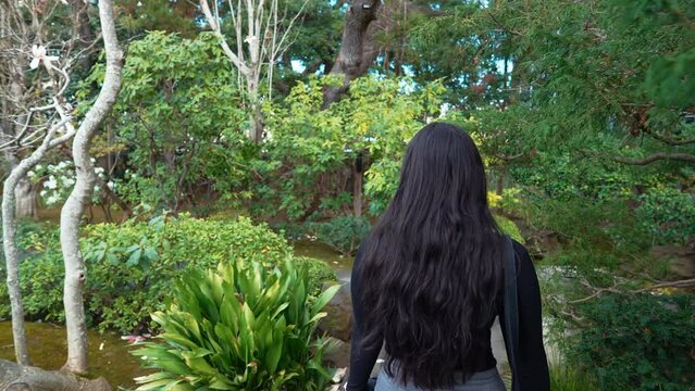 a 4k slow-motion, stabilized video depicting a beautiful young middle eastern female model exploring a lush Japanese Tea Garden walking along a garden path, peninsula, california