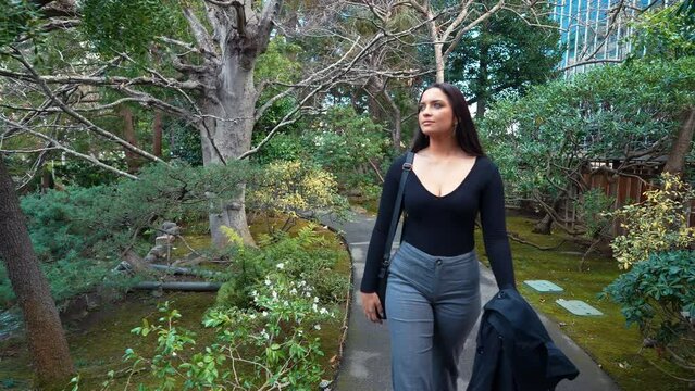 a 4k slow-motion, stabilized video depicting a beautiful young arabic female model exploring a lush Japanese Tea Garden walking along a garden path, peninsula, california