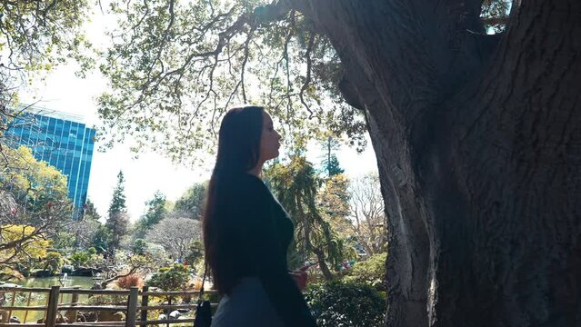 a 4k slow-motion, stabilized video depicting a beautiful young middle eastern female model exploring a lush Japanese Tea Garden slowly moving to touch a tree, peninsula, california.