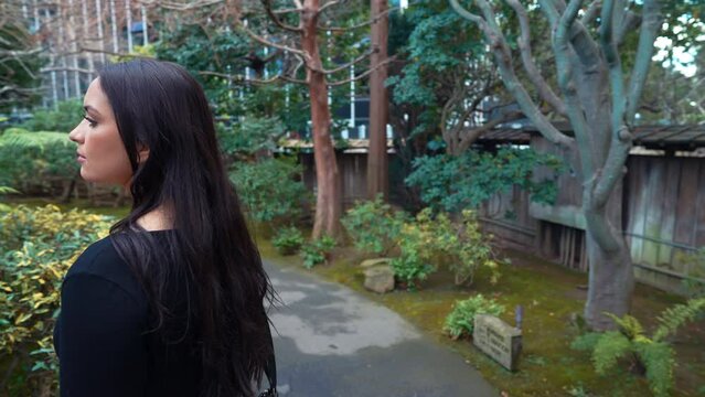 a 4k slow-motion, stabilized video depicting a beautiful young middle eastern female model exploring a lush Japanese Tea Garden walking along a garden path, peninsula, california