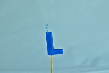 close up on a blue letter L birthday candle on a white background.
