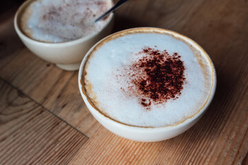 Cup of freshly made delicious cappuccino coffee with fluffy foam and cacao powder on rustic wooden background in modern bar, view from above.