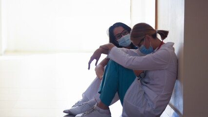 Tired women doctors wearing protective medical masks sitting in clinic corridor. Stress at work of medical staff concept