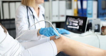 Doctor doing ultrasound examination of patient knee joint in clinic closeup. Instrumental diagnosis of rheumatic diseases concept