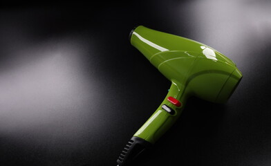 Closeup of green professional hair dryer against dark background. Hair care concept