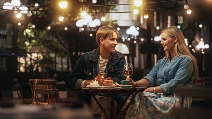 Poster Young Beautiful Couple is Having a Romantic Date at a Cafe at Night. Happy Man and Woman Sitting on a Terrace and Having Fun Conversations During Their Dinner Together in City Center on Weekend © Gorodenkoff