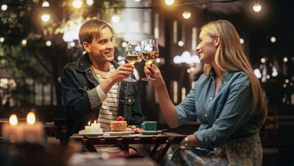 Young Man and Woman Having an Evening Date on a Terrace. Handsome Man Telling Interesting Funny Stories, Beautiful Female Enthusiastically Listening. Couple Toasting and Clinking Glasses with Wine