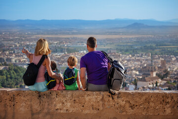 Travelers with kids sit on high wall and enjoy Alhambra view - 755575120