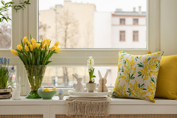 Interior design of spring living room with tulips in vase, easter decorations, pillows on the...